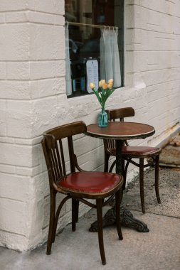 İki ahşap sandalye ve bir vazo çiçekli küçük bir masa bir duvarın yakınındaki kafenin önüne kurulur..
