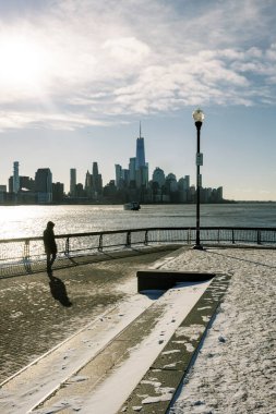 Bir insan şehrin yanındaki suyun yanında yürüyor. Gökyüzü karla kaplı ve güneş ışığı bir kış günü tepede parlıyor..