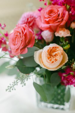 Cam bir vazo, güller ve çiçeklerin bir karışımını barındırır, kapalı alanlarda sergilenir ve yakınlardaki pencerelerden içeri ışık saçar..