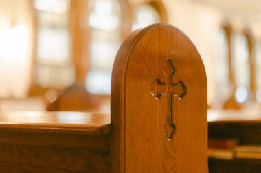 Ahşap kilise sırası, gün boyunca yumuşak ışıkla dolu bir ibadethanede haç oyması gösteriyor..