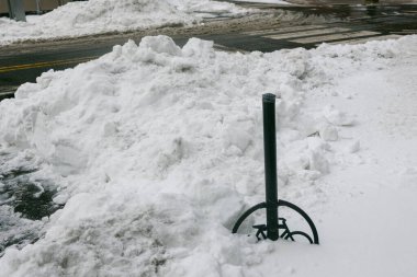 Kar zemini kaplıyor ve caddeye yakın yığılıyor. Bu kış sahnesinde karların arasında metal bir direk duruyor..