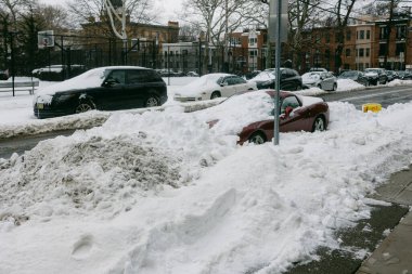 Kar yığınları, soğuk bir kış günü şehirde yol boyunca park halindeki arabaların manzarasını engelliyor..