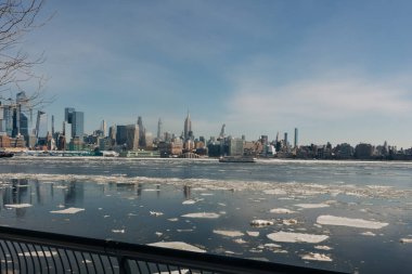 New York şehrinin silueti, kışın parlak bir gökyüzünün altında nehirde yüzen buzla kaplı binaları gösteriyor..