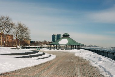 Bir çardak karla kaplı bir patikanın üzerinde duruyor. Bir kış günü, deniz kenarında binalar var..