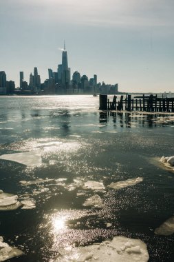 Su, kış boyunca New York 'un ufuk çizgisi yakınlarındaki nehirde yüzen büyük buz parçaları gibi güneş ışığını yansıtır..