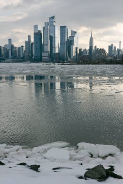 Kış mevsiminde New York 'ta binaları yansıtan buzla kaplı sular üzerinde şehrin ufuk çizgisi beliriyor..