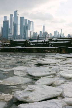 New York 'un ufuk çizgisi bulutlu gökyüzünün altında bir kış günü boyunca durdukça buz nehirde yüzer..