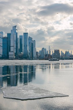 Suyun üzerindeki yüksek binaları ve buzları gösteren bir şehir manzarası. Kışın bulutlu bir gün..