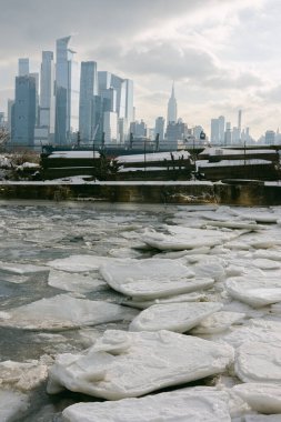 New York 'ta soğuk bir kış gününde arka planda yüksek binalar görülürken, kar ve buz nehri kaplıyor.