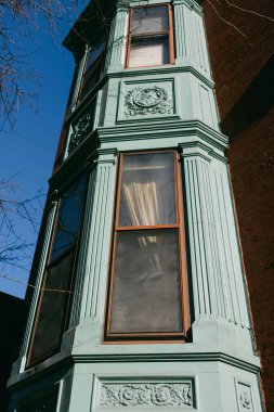 Binanın köşesinde güneşli bir havada birkaç pencereli yeşil ahşap işçiliği görülüyor. Yapının detaylı tasarımı var..