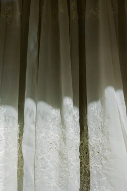 Beyaz perdeler bir odada asılı. Güneş ışığı filtrelenip gölgeler oluştururken ve uzayda sıcak bir parıltı yaratırken..