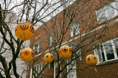 Yüzleri çıplak dallardan sarkan sarı yuvarlak dekorasyonlar sonbaharda bulutlu bir günde tuğla bir binanın yanında..