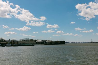 Sahnede limanda birkaç bina ve tekne olan bir rıhtım var. Gökyüzü bulutlarla mavidir. Su sakin ve bölge gündüzleri hareketlilikle dolu..