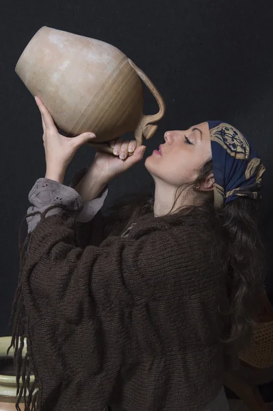 Vrouw met omslagdoek en hoofd bedekt drinken uit een ' Amfora — Stockfoto