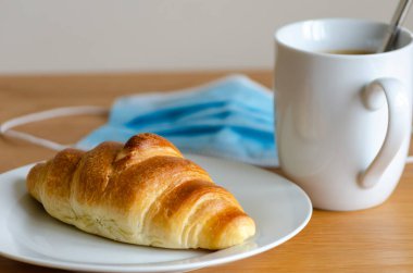 Kapalı kruvasan mavi renkli maske ve beyaz bıçaklı kahve ve kırmızı masa örtüsü seçici odaklı.