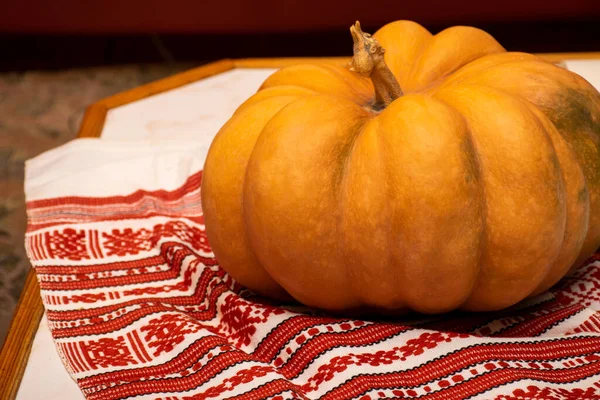 Abóbora laranja madura e brilhante fica em uma toalha de mesa tecida em casa na mesa da cozinha. — Fotografia de Stock