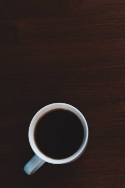 Koyu ışık modunda, ahşap masada bir fincan kahve.