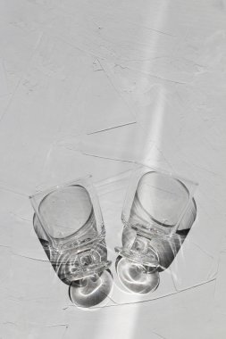 Güneş ışınları ve yansımaları olan gri beton bir masa üzerindeki cam, yukarıdan görüş, soyut gölgeler ve güneş ışığı