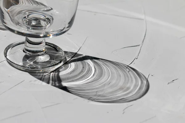 Glass on a grey concrete table with sunbeams and reflections, view from above, abstract shadows and sunlight