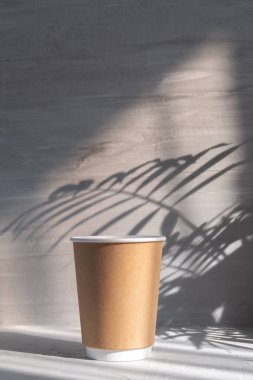 Boş kağıt bardak, gri beton arka planda, palmiye yaprağı gölgesinde.