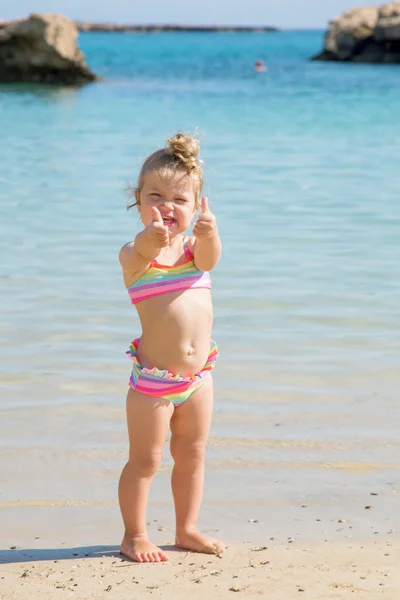 Liten flicka visar tummen på stranden. — Stockfoto