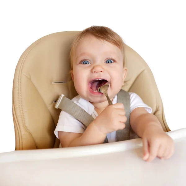 Baby eating with spoon in high chair — Stock Photo, Image