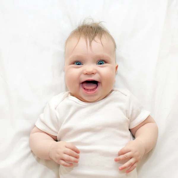 Smiling surprised baby lying on a white bed. — Stock Photo, Image