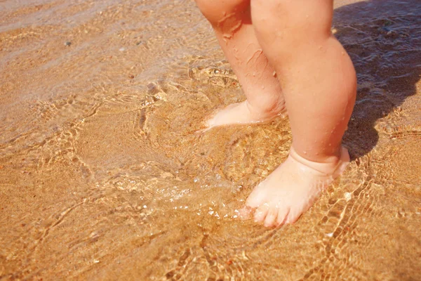 Baby fötter i vattnet vid sandstrand — Stockfoto