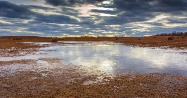 Весенние поля с замерзшим прудом, облачные отражения на льду — стоковое видео