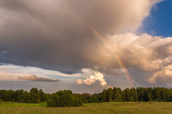 Радуга над бурным небом. Сельский пейзаж с радугой над темным бурным небом в сельской местности в летний день. — стоковое фото
