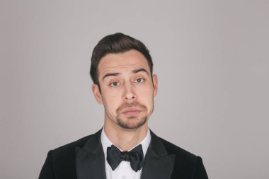 Smokinli genç beyaz bir adamın stüdyo portresi, düz stüdyo arka planında, kameraya bakarak bir yüz yapar