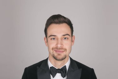 Smokinli genç beyaz bir adamın stüdyo portresi, gülümsüyor, kameraya bakıyor.