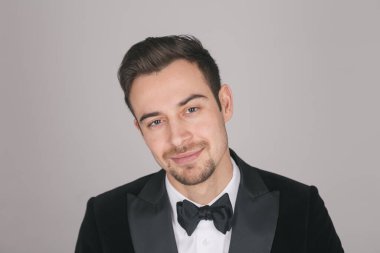 Smokinli genç beyaz bir adamın stüdyo portresi, gülümsüyor, kameraya bakıyor.