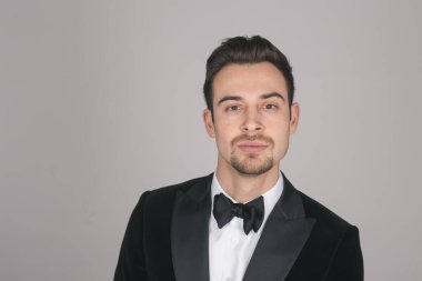 Smokinli genç beyaz bir adamın stüdyo resmi, kameraya bakıyor, stüdyo arka planına bakıyor.