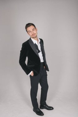 Smokinli genç beyaz bir adamın stüdyo portresi, kameraya bakıyor, düz stüdyo arka planında duruyor.