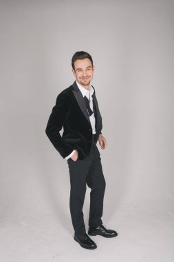 Smokinli genç beyaz bir adamın stüdyo portresi, kameraya bakıyor, düz stüdyo arka planında duruyor.