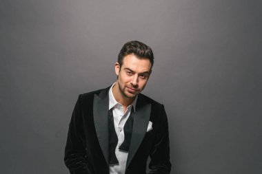 Smokinli genç beyaz bir adamın stüdyo resmi, kameraya bakıyor, stüdyo arka planına bakıyor.