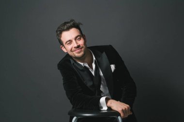 Smokinli genç beyaz bir adamın stüdyo portresi, gülümsüyor, kameraya bakıyor.