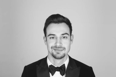 Smokinli genç beyaz bir adamın stüdyo portresi, gülümsüyor, kameraya bakıyor.