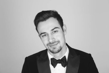 Smokinli genç beyaz bir adamın stüdyo portresi, gülümsüyor, kameraya bakıyor.