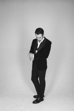 Smokinli genç beyaz bir adamın stüdyo portresi, aşağı bakıyor, düz stüdyo arka planında duruyor.