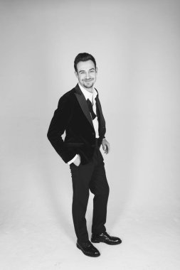 Smokinli genç beyaz bir adamın stüdyo portresi, kameraya bakıyor, düz stüdyo arka planında duruyor.