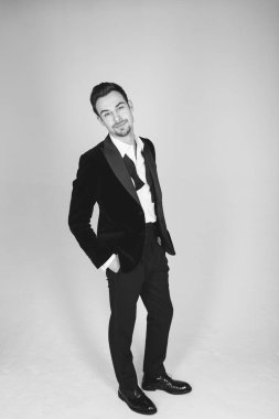 Smokinli genç beyaz bir adamın stüdyo portresi, kameraya bakıyor, düz stüdyo arka planında duruyor.