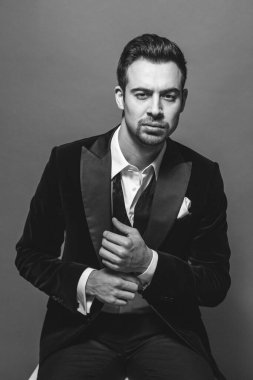 Smokinli genç beyaz bir adamın stüdyo resmi, kameraya bakıyor, stüdyo arka planına bakıyor.