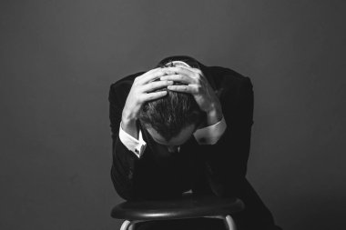 Smokinli genç beyaz bir adamın stüdyo portresi, elleri saçlarında, ne yazık ki düz stüdyo arka planına bakıyor.