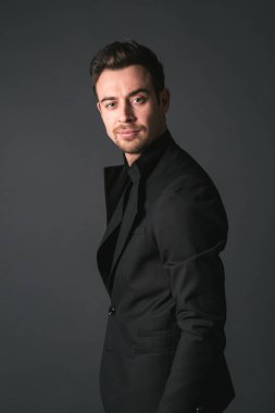 Siyah ceketli genç beyaz bir adamın stüdyo portresi, kameraya bakıyor, yarım yamalak bir şekilde stüdyonun arka planına bakıyor.