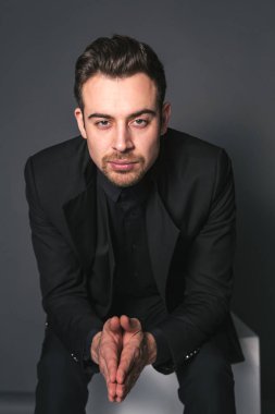 Siyah ceketli beyaz bir adamın stüdyo portresi. Stüdyonun arka planında kameraya bakıyor.