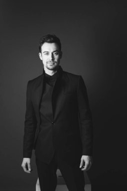 Siyah ceketli beyaz bir adamın stüdyo portresi. Kameraya bakıyor. Stüdyonun arka planında duruyor.