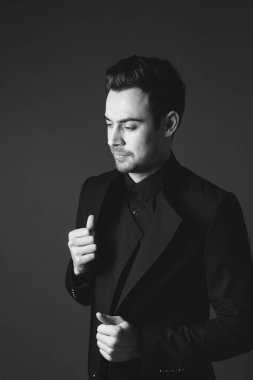 Siyah ceketli genç beyaz bir adamın stüdyo portresi, yan bakıyor, yarım düz stüdyo arka planı karşı ayakta