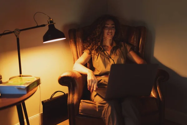 Gambar Seorang Wanita Tersenyum Melihat Layar Laptop Sambil Duduk Kursi — Stok Foto